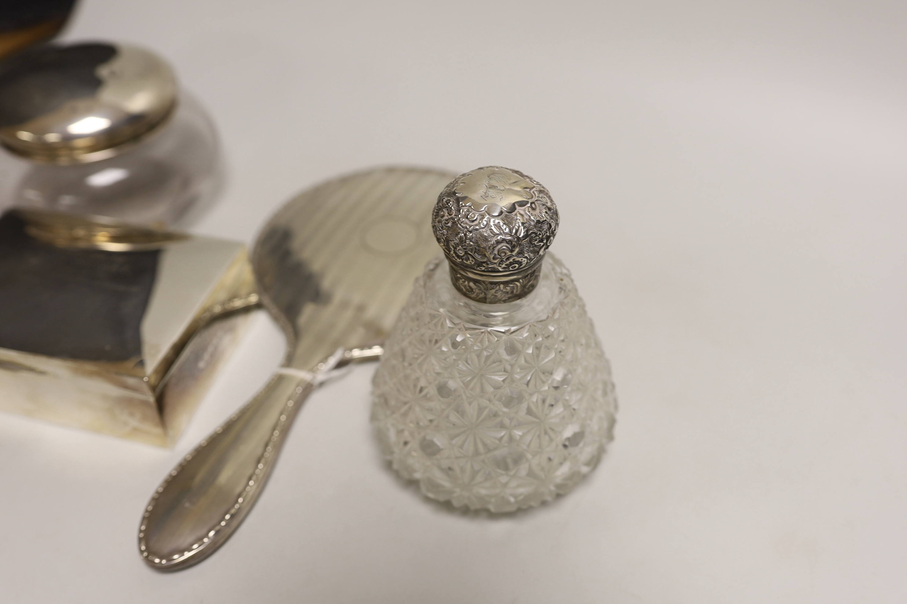 A George V silver backed hand mirror, a silver mounted cigarette box, a silver topped powder bowl and a silver topped scent bottle.